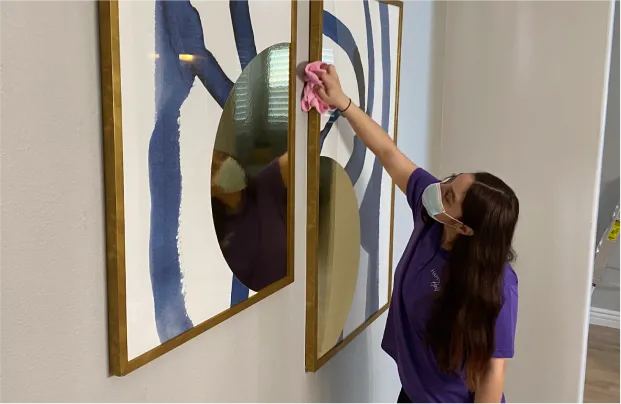 Female cleaner in a blue uniform and gloves wiping dust from the painting in Upper East Side Manhattan residence
