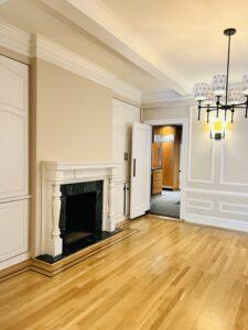 A pristine, freshly cleaned pre-war luxury apartment living room on the Upper West Side of Manhattan after a move-out cleaning service by ELcleaning, featuring polished hardwood floors and an elegant fireplace.
