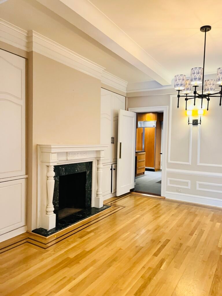 A pristine, freshly cleaned pre-war luxury apartment living room on the Upper West Side of Manhattan after a move-out cleaning service by ELcleaning, featuring polished hardwood floors and an elegant fireplace.
